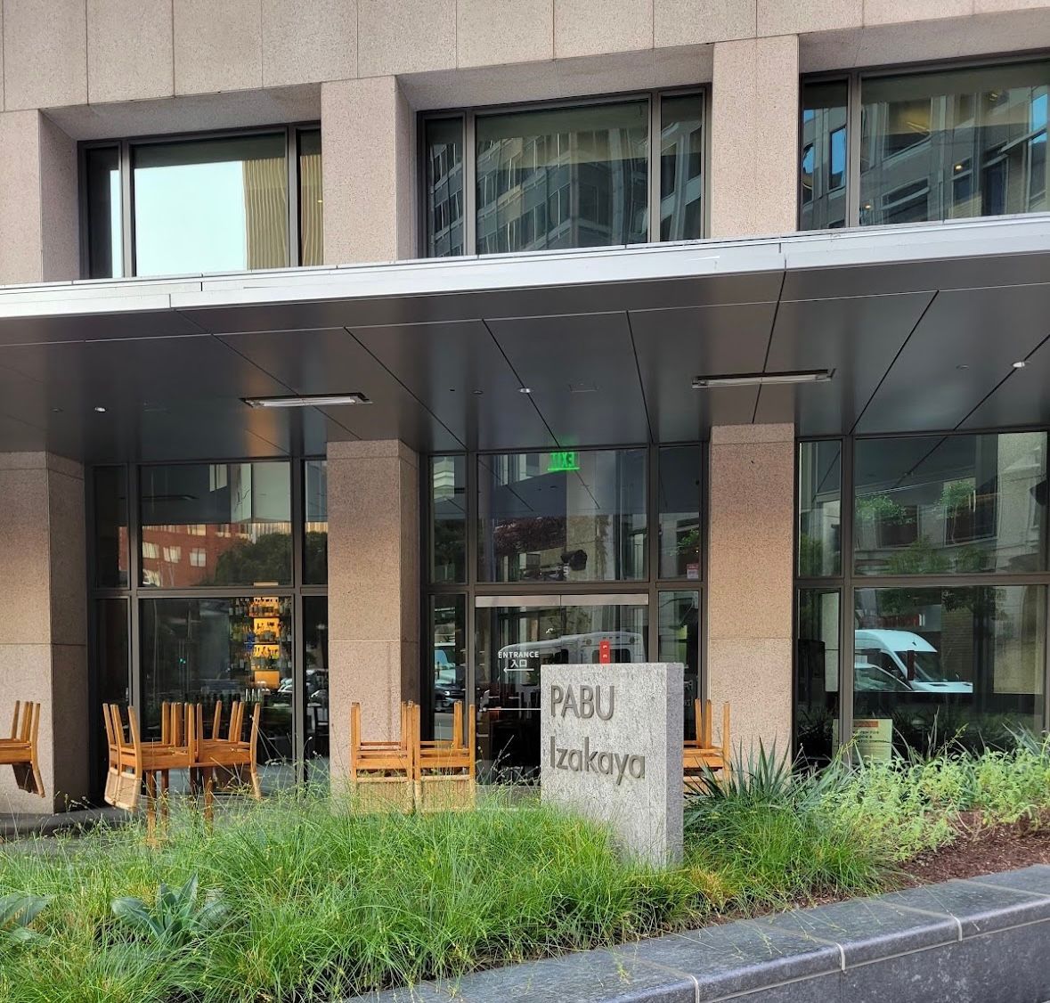 Modern glass building entrance with café seating and a stone sign in front