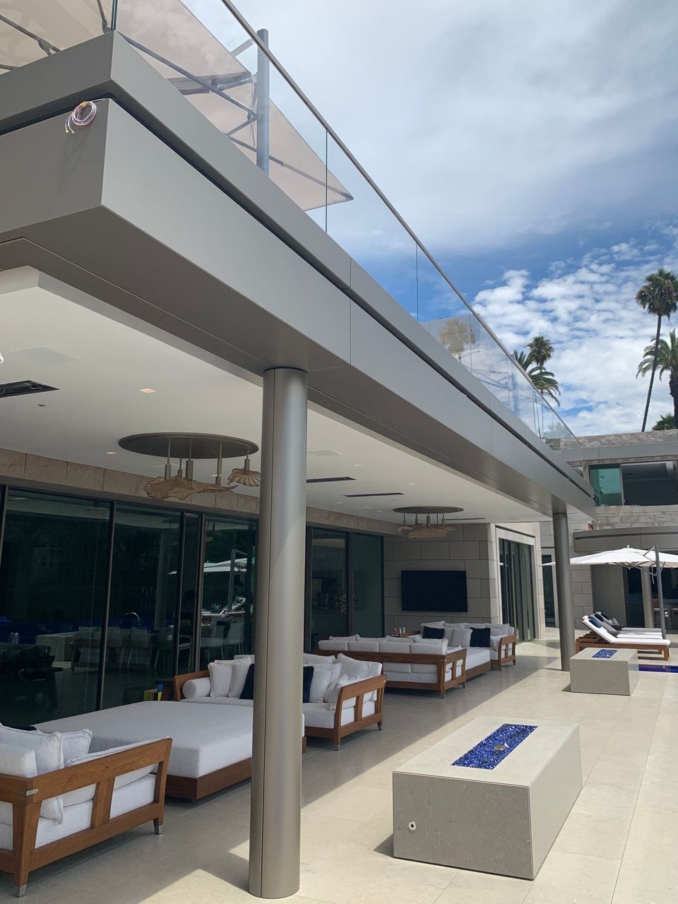 Modern outdoor lounge with white sofas, wooden tables, and a poolside terrace under a blue sky