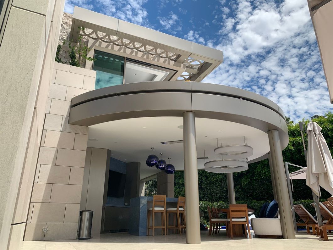 Modern house patio with curved white canopy, columns, wooden table, and blue sky overhead