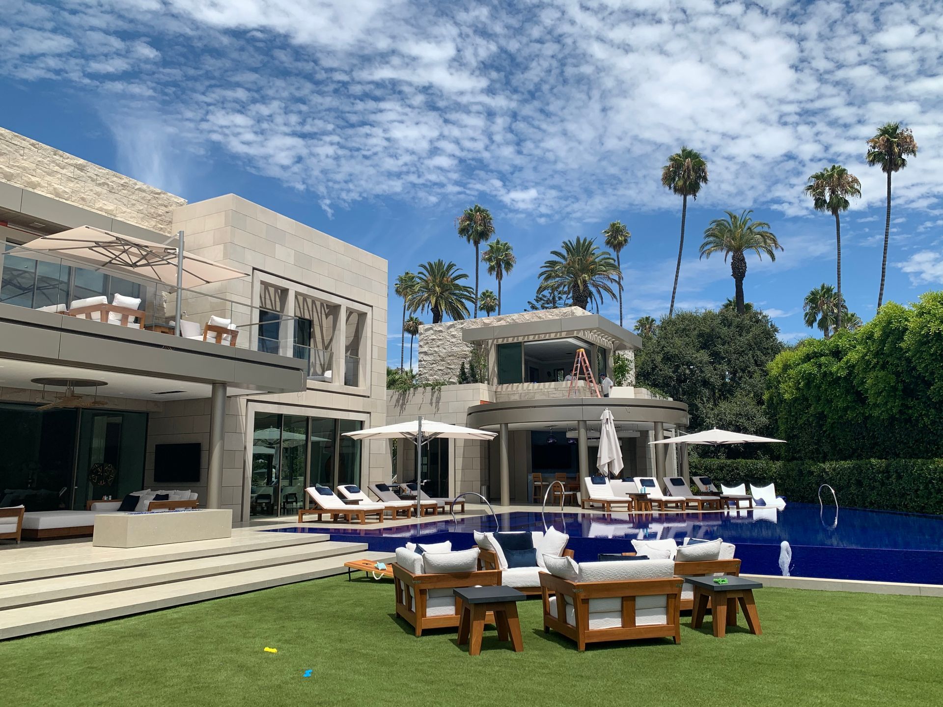 Modern villa with poolside lounge seating, blue water, and palm trees under a bright sky