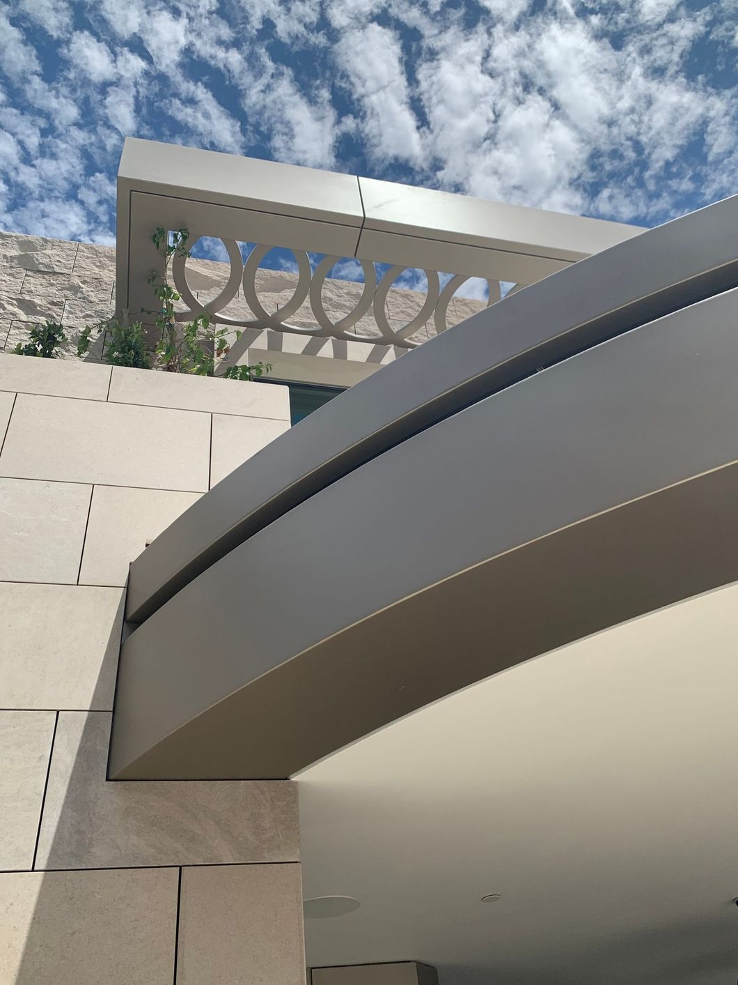 Modern building facade with curved overhang and decorative metal railing against a cloudy sky