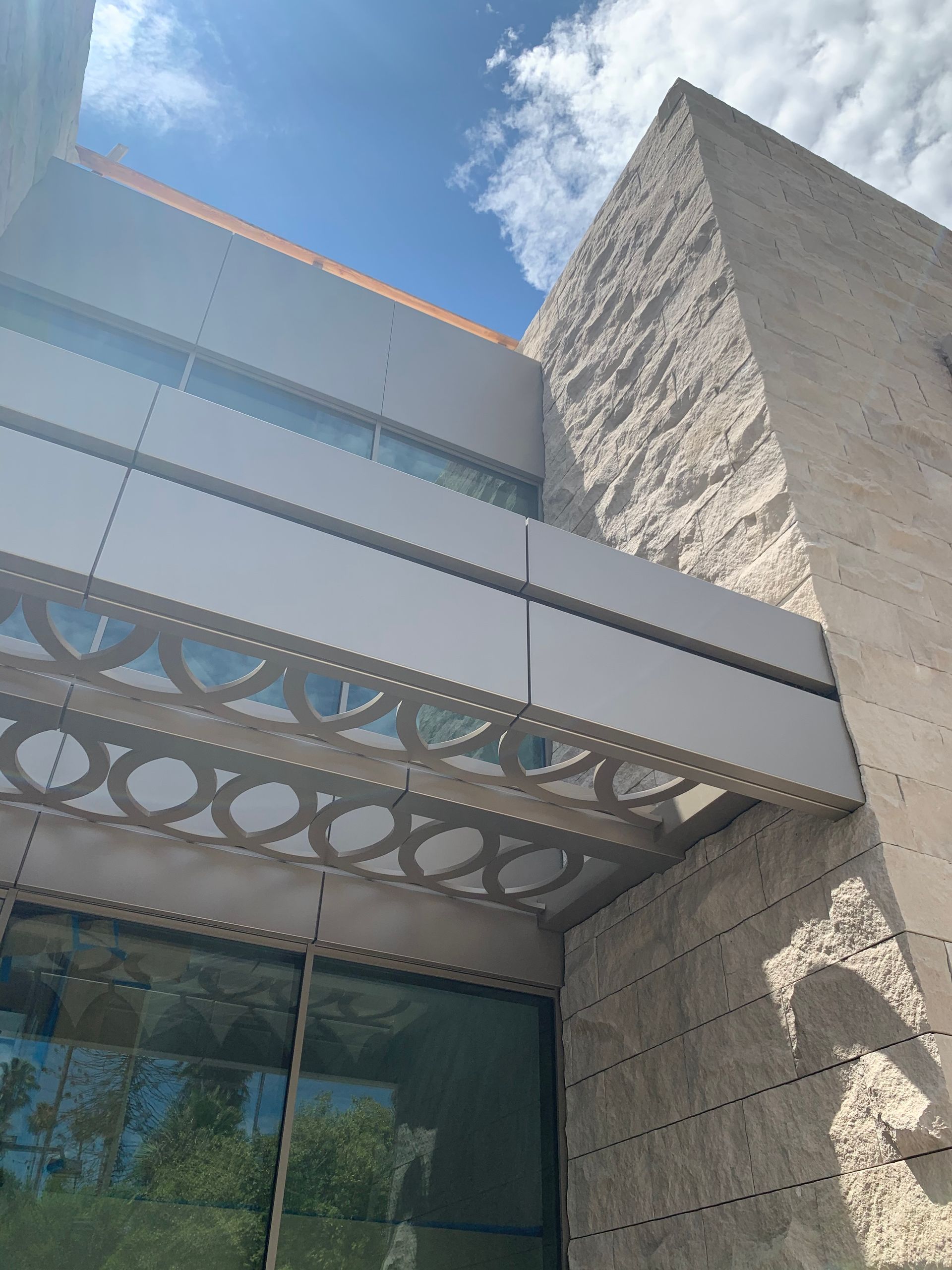Modern building entrance with stone walls, glass facade, and decorative metal canopy under a blue sky