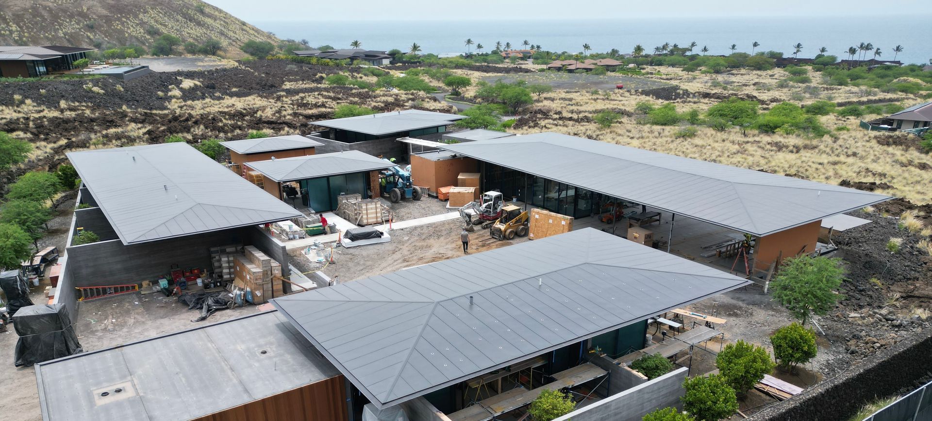 Aerial view of a modern open-air building complex with gray roofs in a rocky coastal landscape