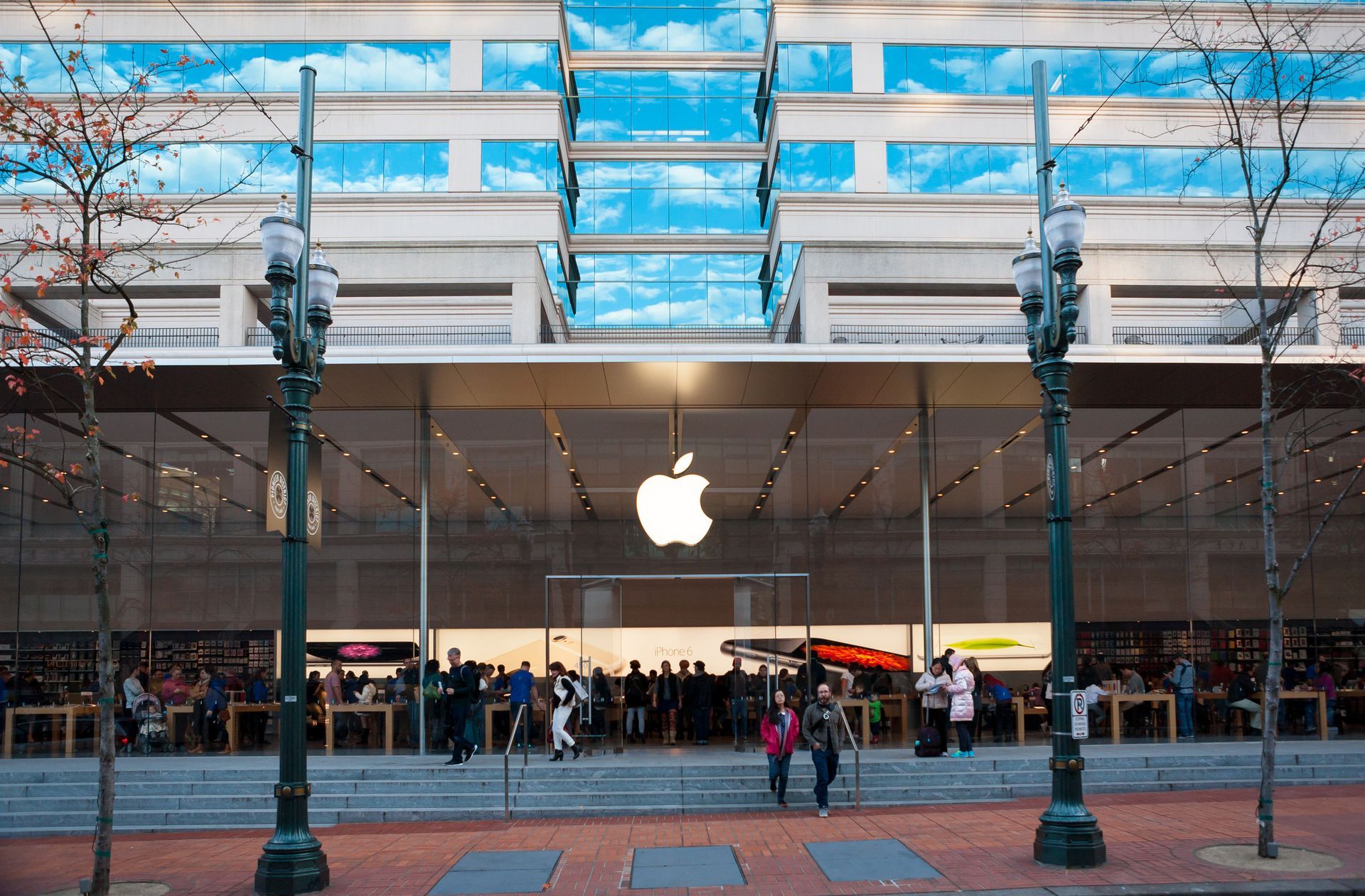 Apple Store storefront with illuminated logo, glass façade, and people gathered outside on a city street