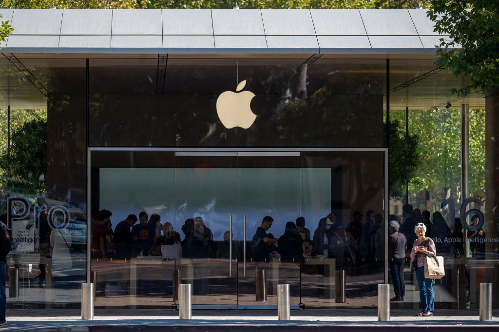 Apple Store glass storefront with logo, reflecting people standing outside and inside.