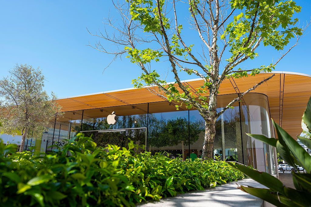 Modern building with orange roof, glass walls, and lush green landscaping under a bright blue sky