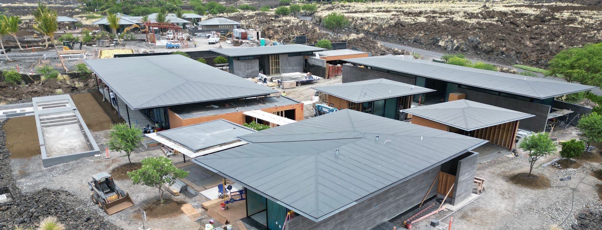 Aerial view of a modern desert-style building complex with gray roofs and surrounding construction materials.