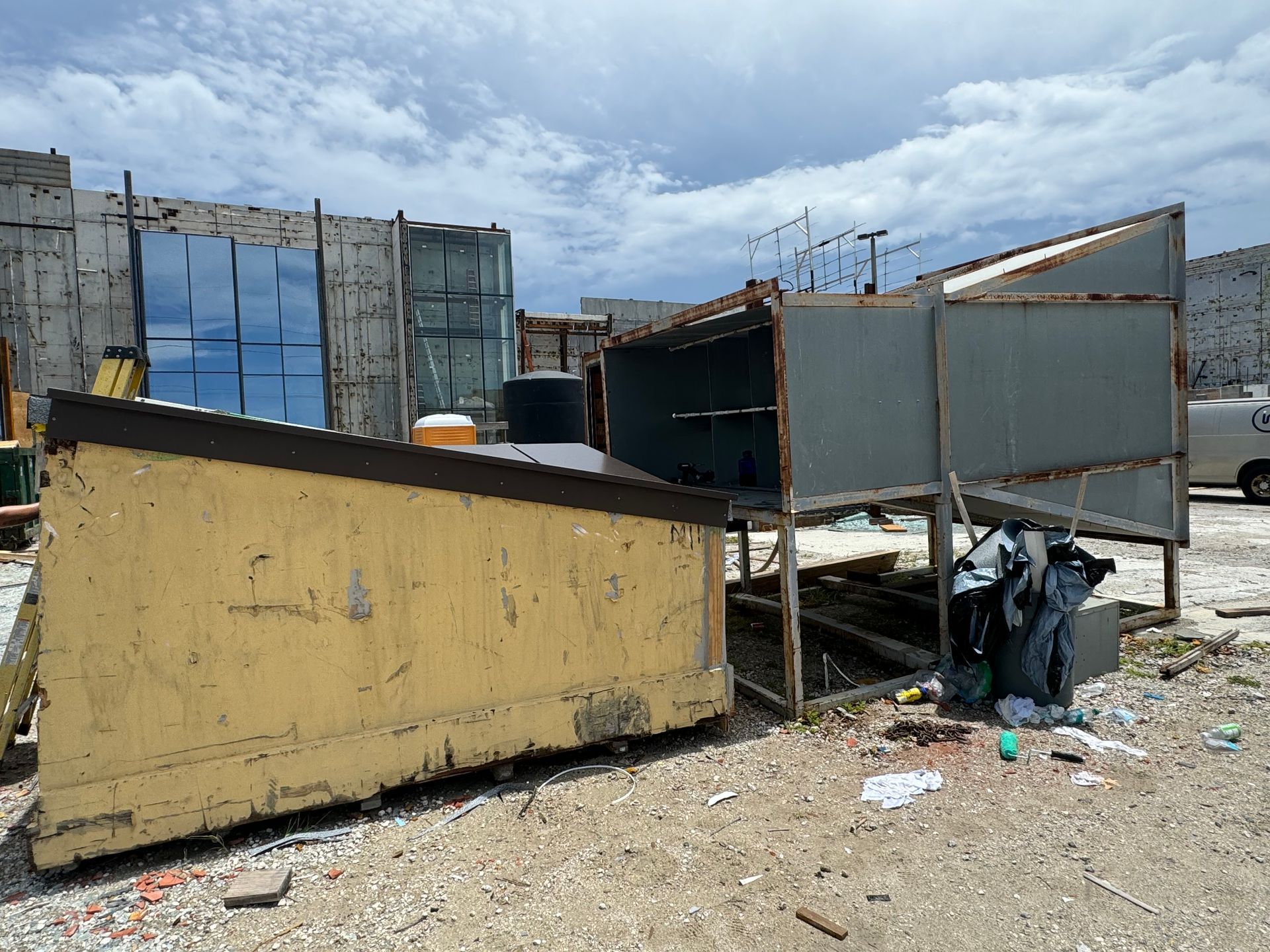 Makeshift corrugated metal shacks and debris in a dusty outdoor settlement under a cloudy sky