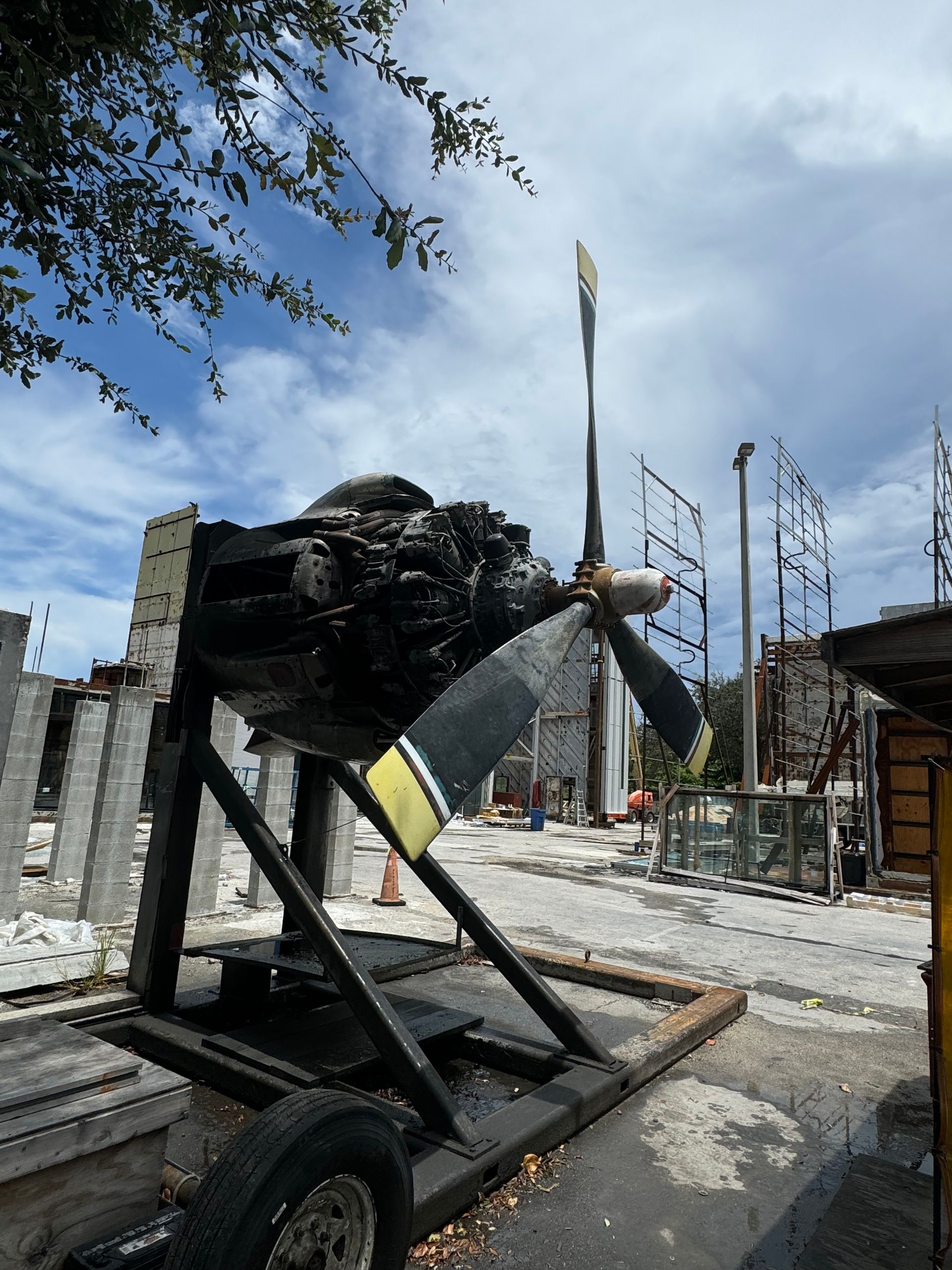 Burned-out vehicle frame on a trailer at a damaged construction site under a clear sky