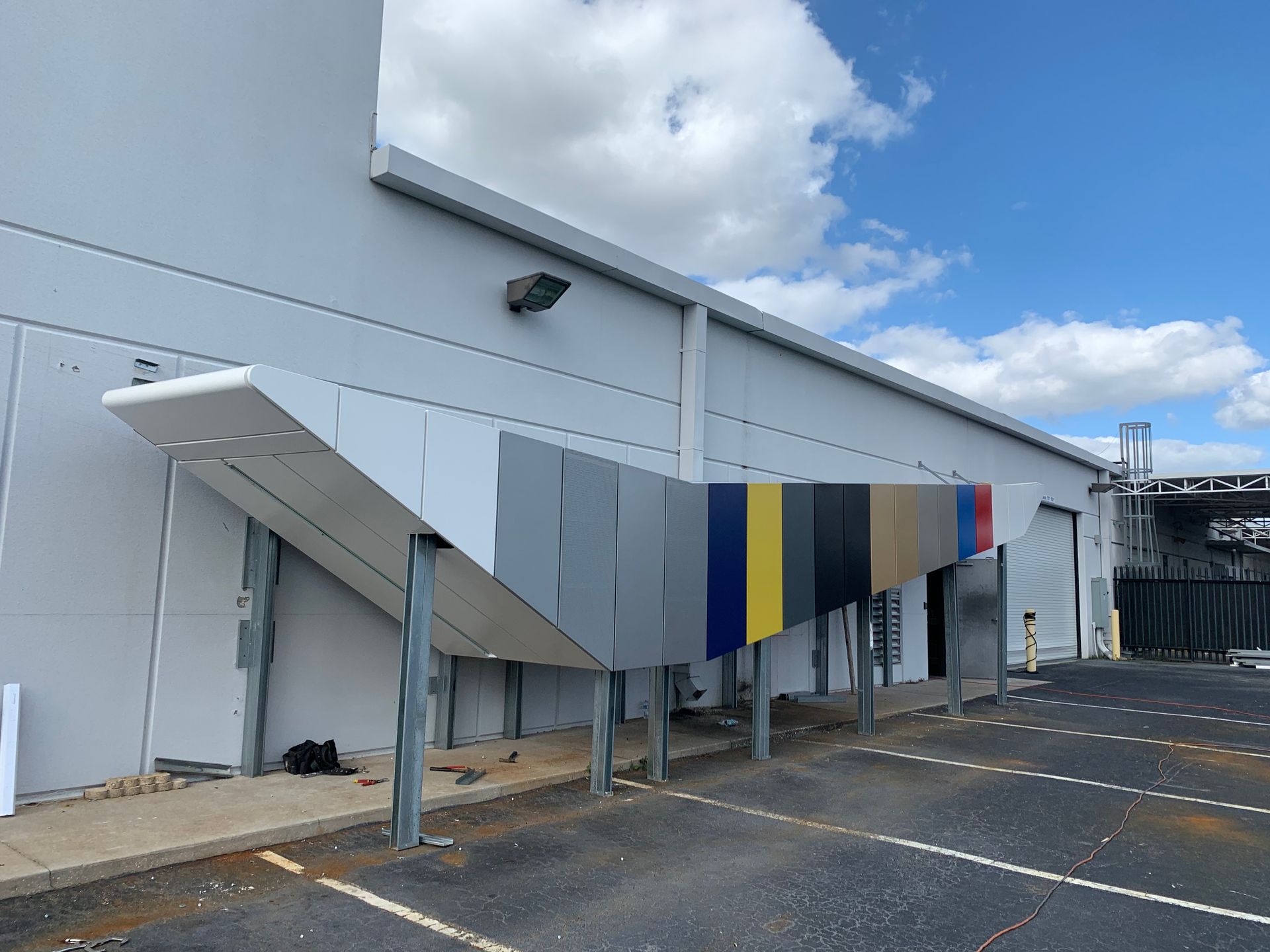 Exterior of a building with a ramp, striped panels, and an empty parking lot under a cloudy sky