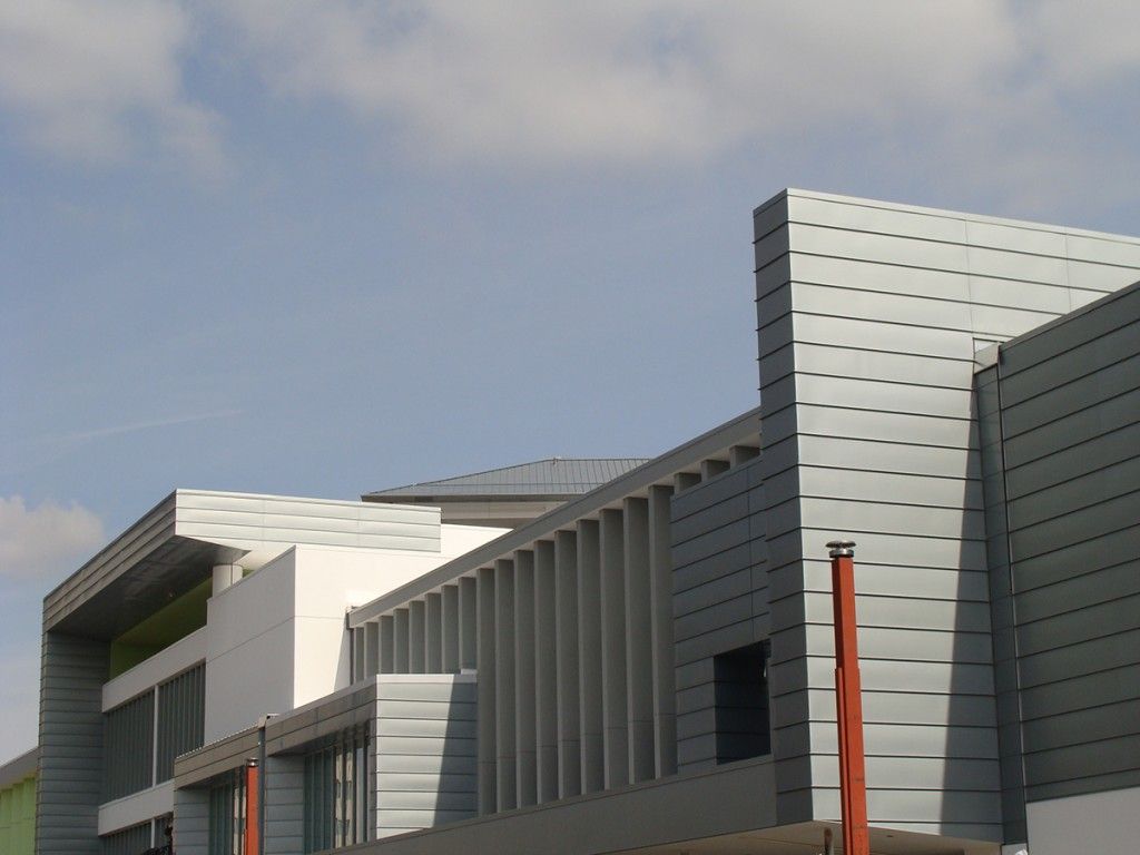 Modern building exterior with gray metal panels and a red pole under a cloudy sky