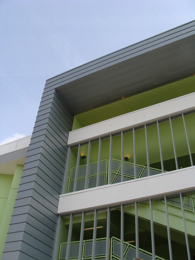 Modern building facade with green-tinted windows and white metal bars against a blue sky