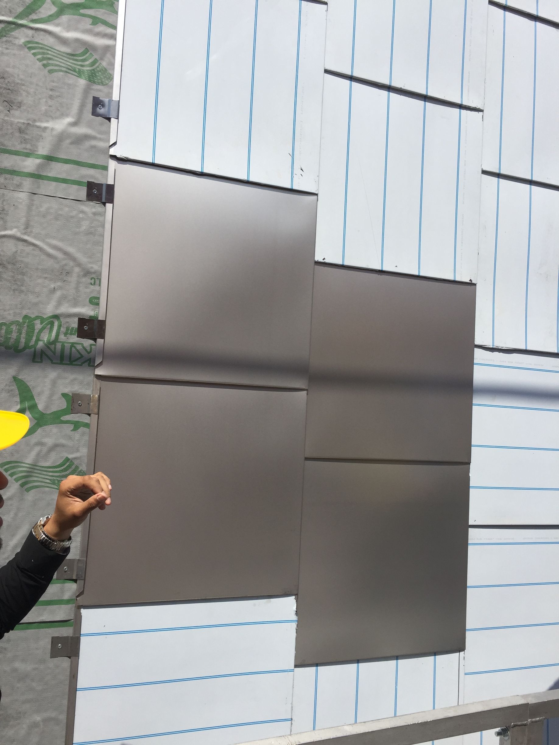 Hands installing or aligning gray rectangular panels on a striped wall surface.