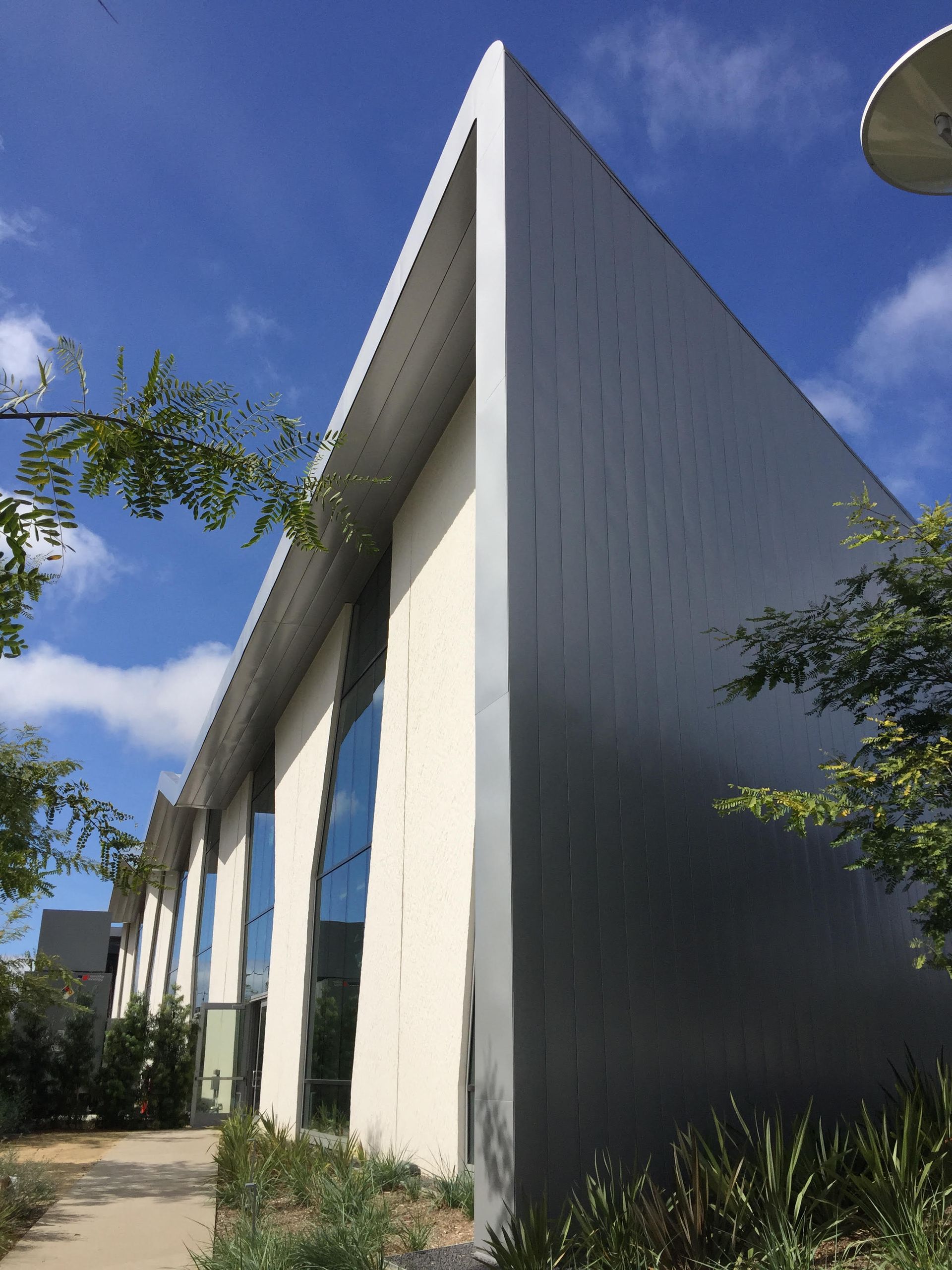 Modern building facade with tall white walls and large windows under a blue sky