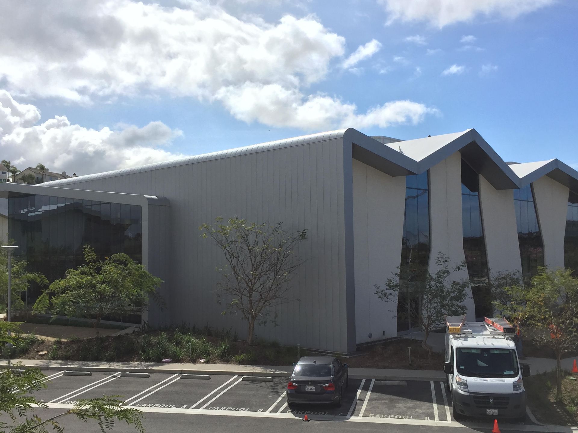 Modern office building with angled rooflines, parked cars, and a partly cloudy sky