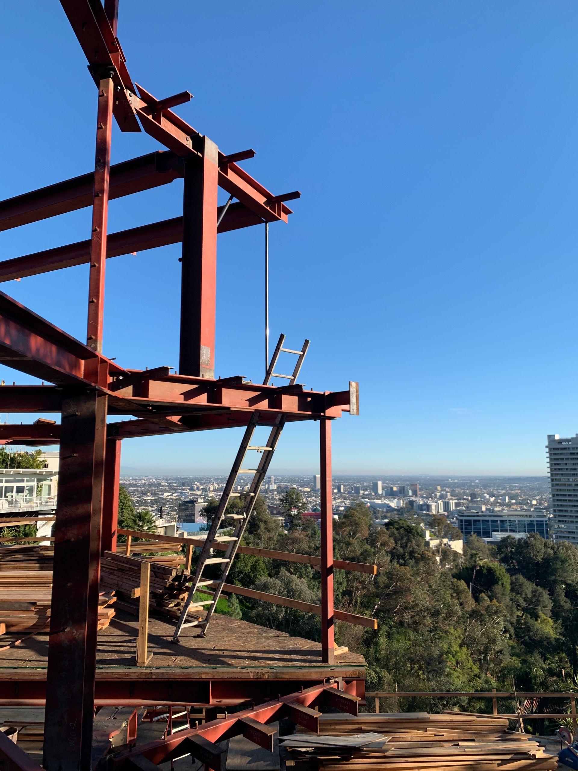 Rust-colored steel building frame overlooking a cityscape under a clear blue sky