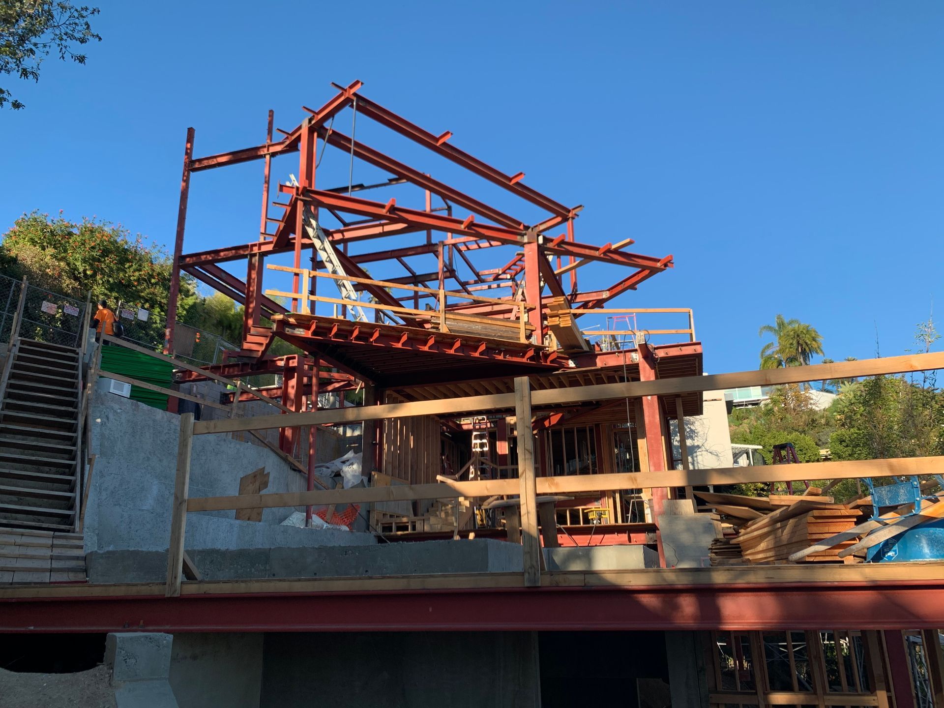 Partially built steel structure with red beams on a construction site under a clear blue sky