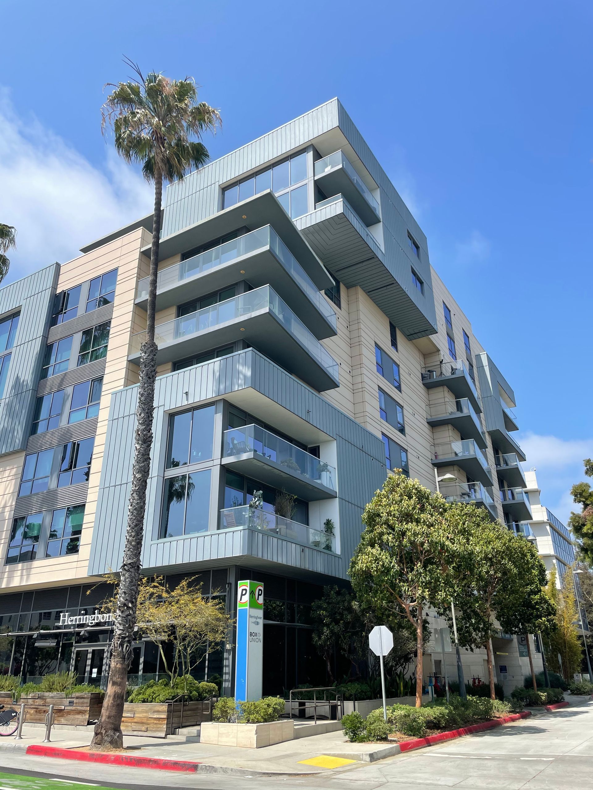 Modern blue-and-white apartment building with balconies on a sunny street corner