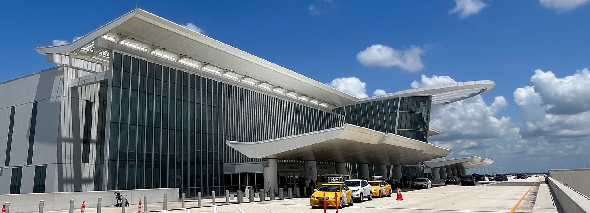 Modern glass-fronted airport terminal with a yellow shuttle bus under a bright blue sky