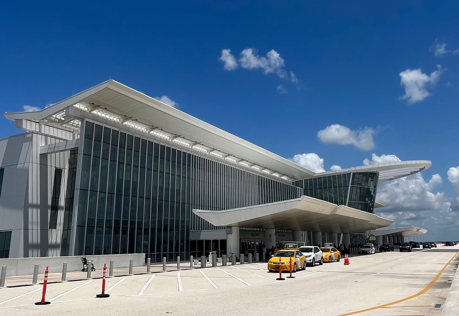 Modern airport terminal with glass facade and a yellow taxi under a blue sky
