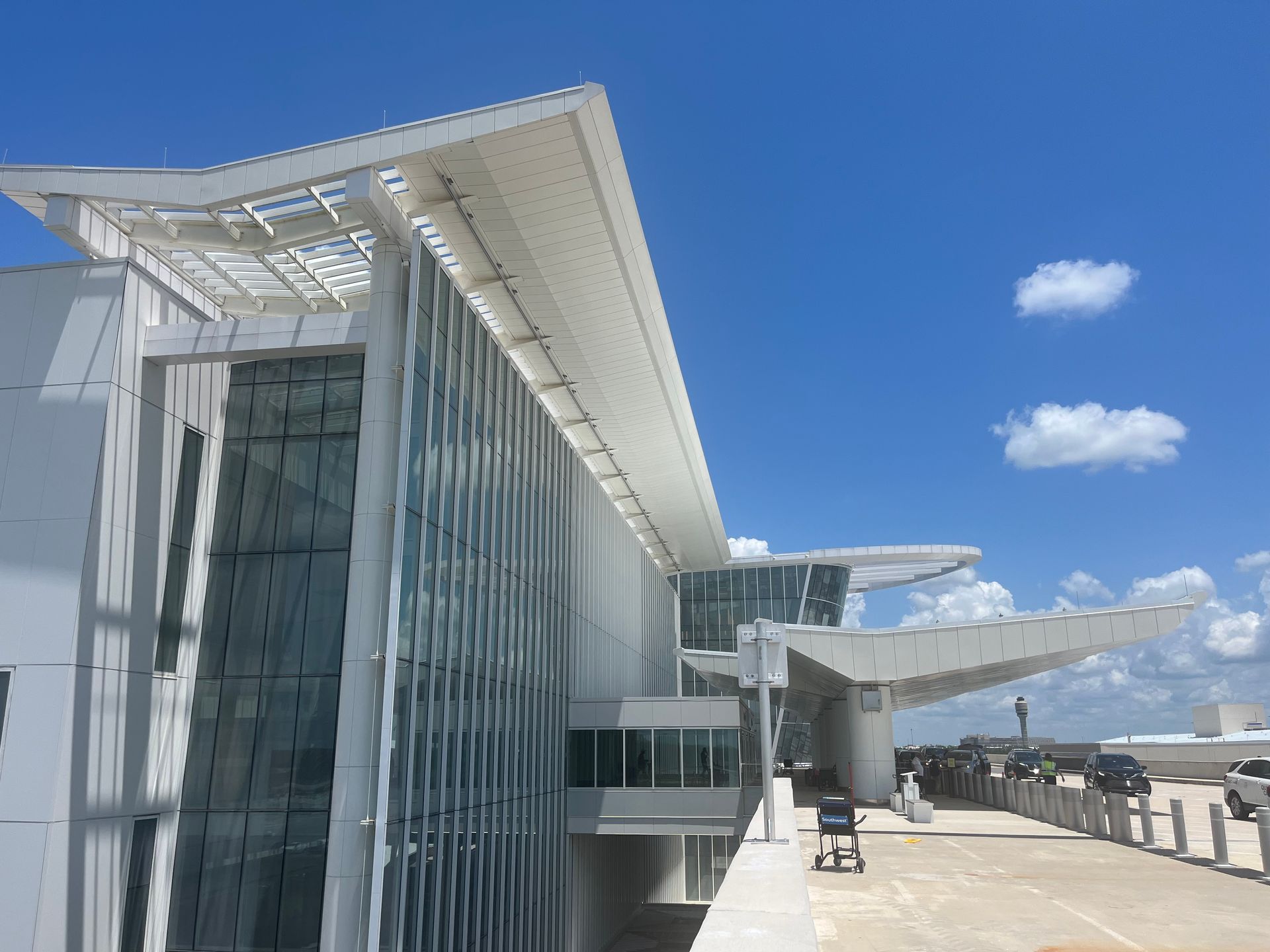 Modern airport terminal with white angular roof, glass facade, and jet bridge under a blue sky
