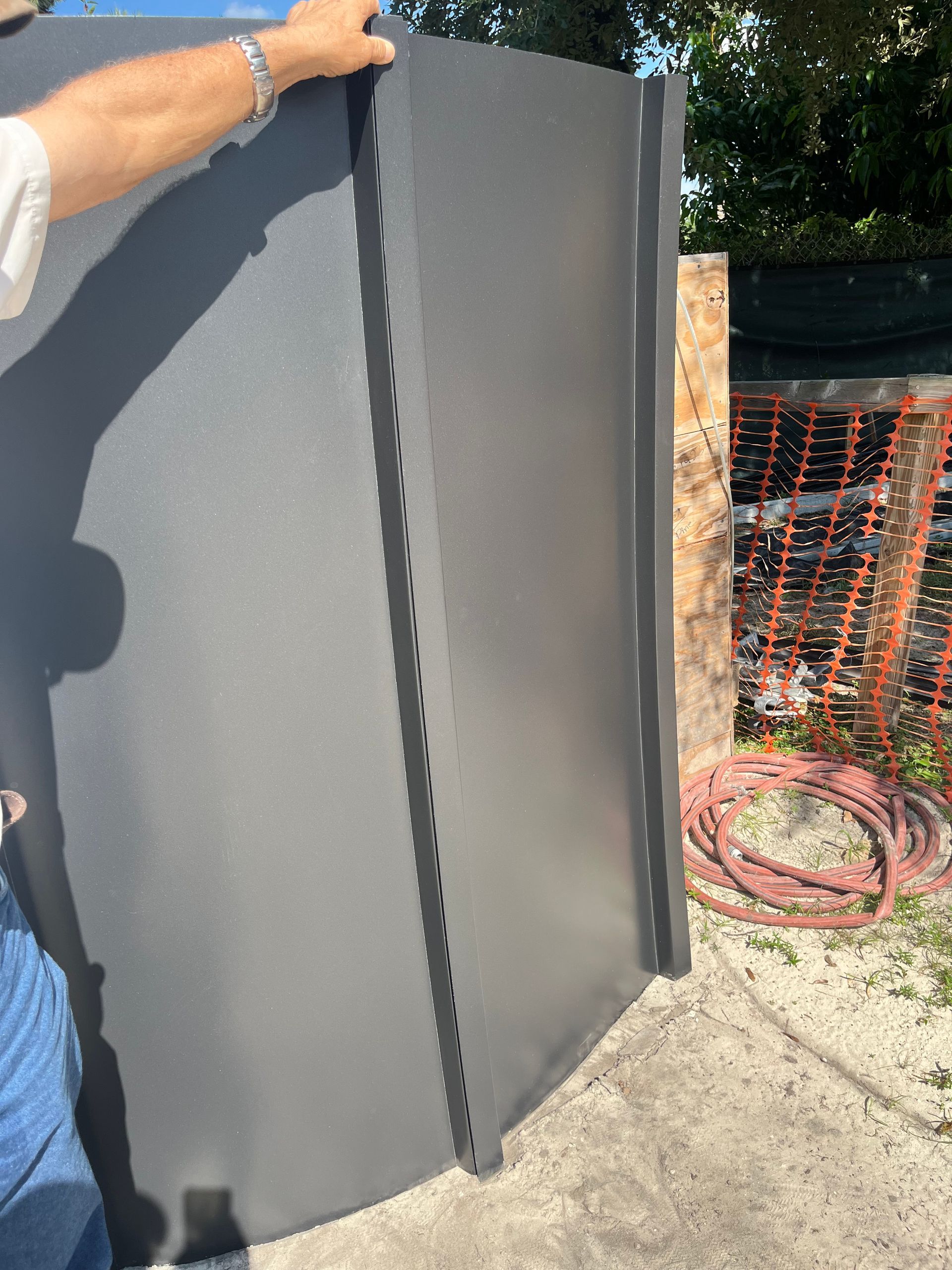 Person holding a large gray panel outdoors on a sunny construction site