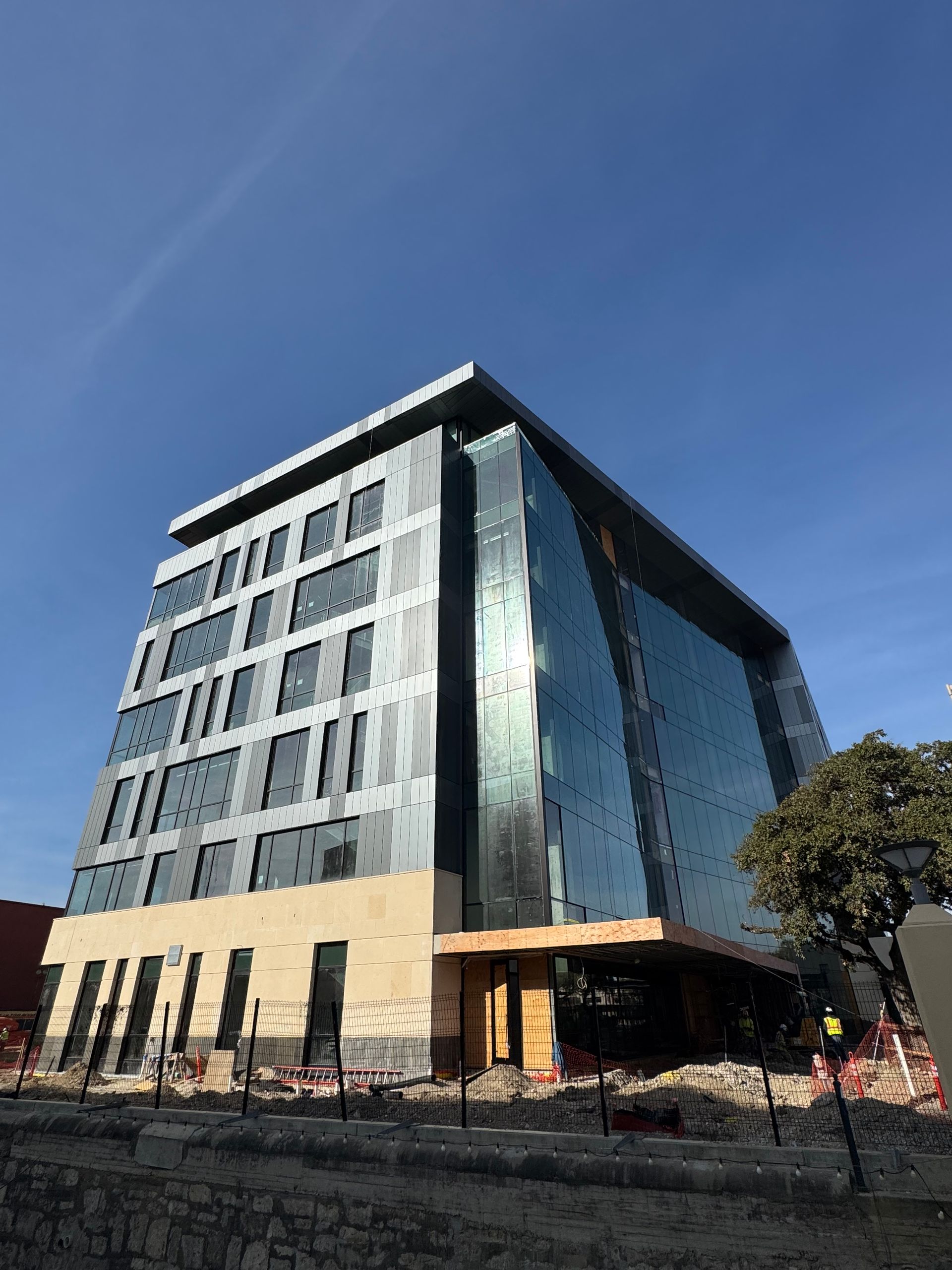 Modern glass office building with beige lower facade under a clear blue sky