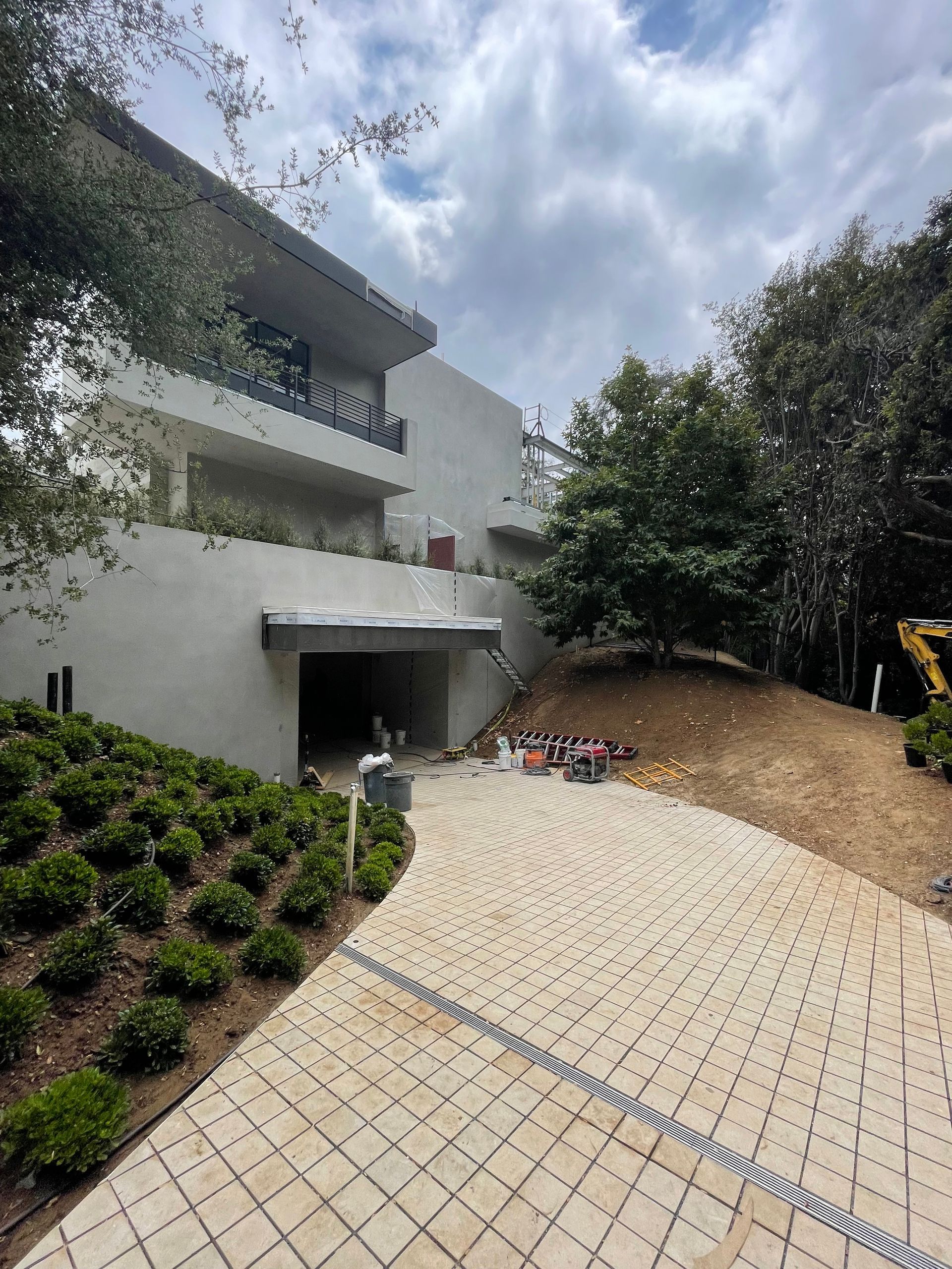 Modern building with terraces beside a sloped paved courtyard and trees under a cloudy sky