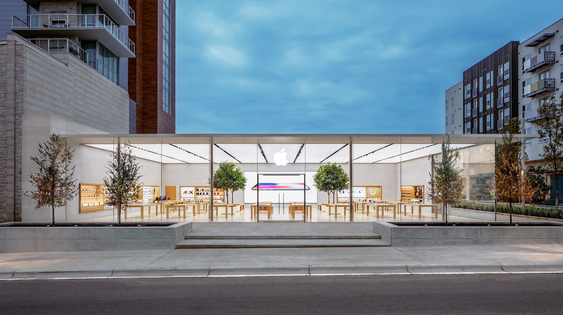 Modern outdoor plaza with a white canopy, benches, trees, and apartment buildings at dusk