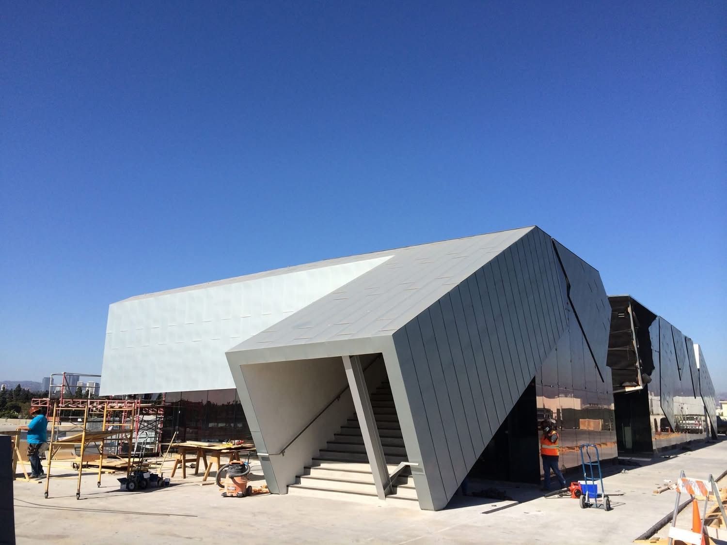 Modern angular building facade with gray panels and a recessed entrance under construction on a sunny site