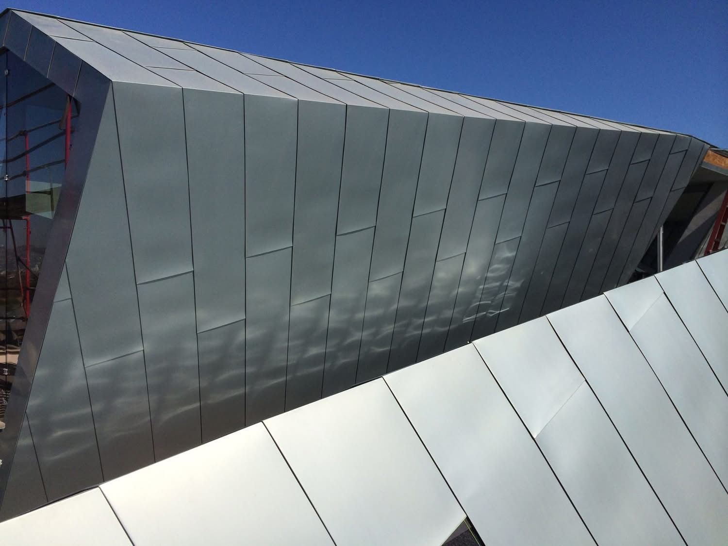 Modern angular metal building under a clear blue sky, with reflective silver panels