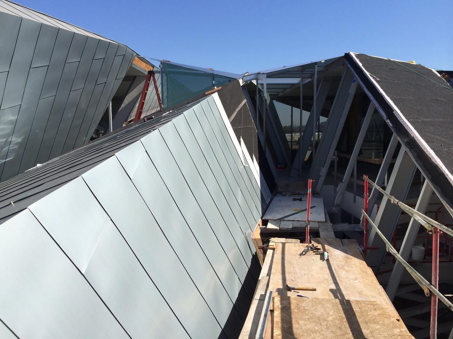 Metal rooftop installation with gray panels, scaffolding, and a central walkway under construction