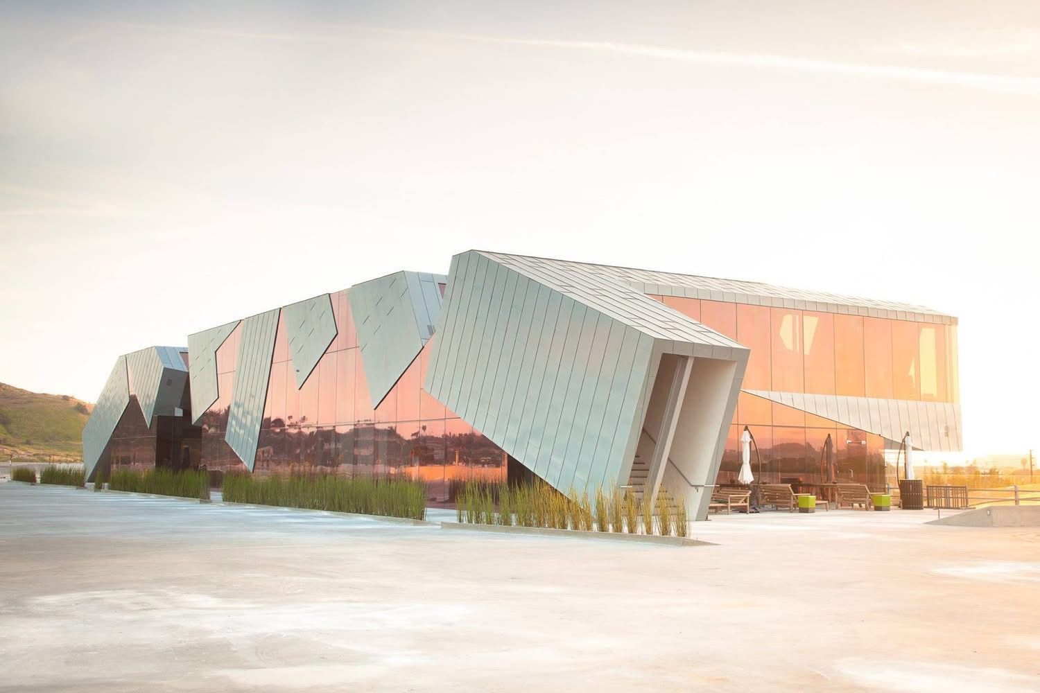 Modern angular building with pink reflective glass and patterned metal panels in an open plaza