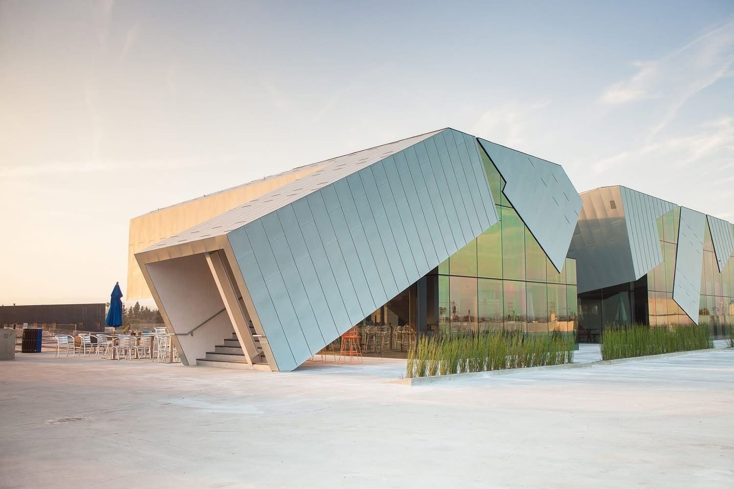 Modern angular building with teal panels and glass facades in a bright open plaza