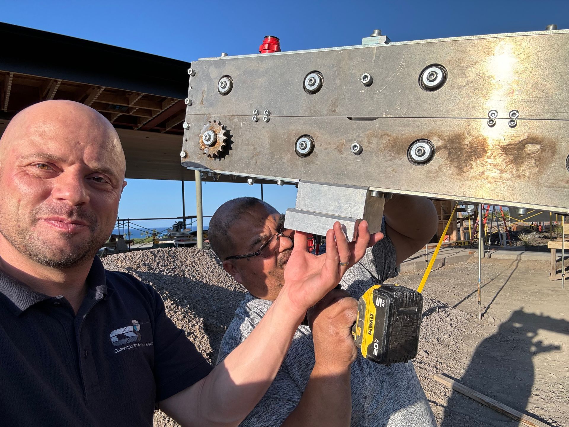 Two men inspecting a large metal beam with bolts at an outdoor construction site