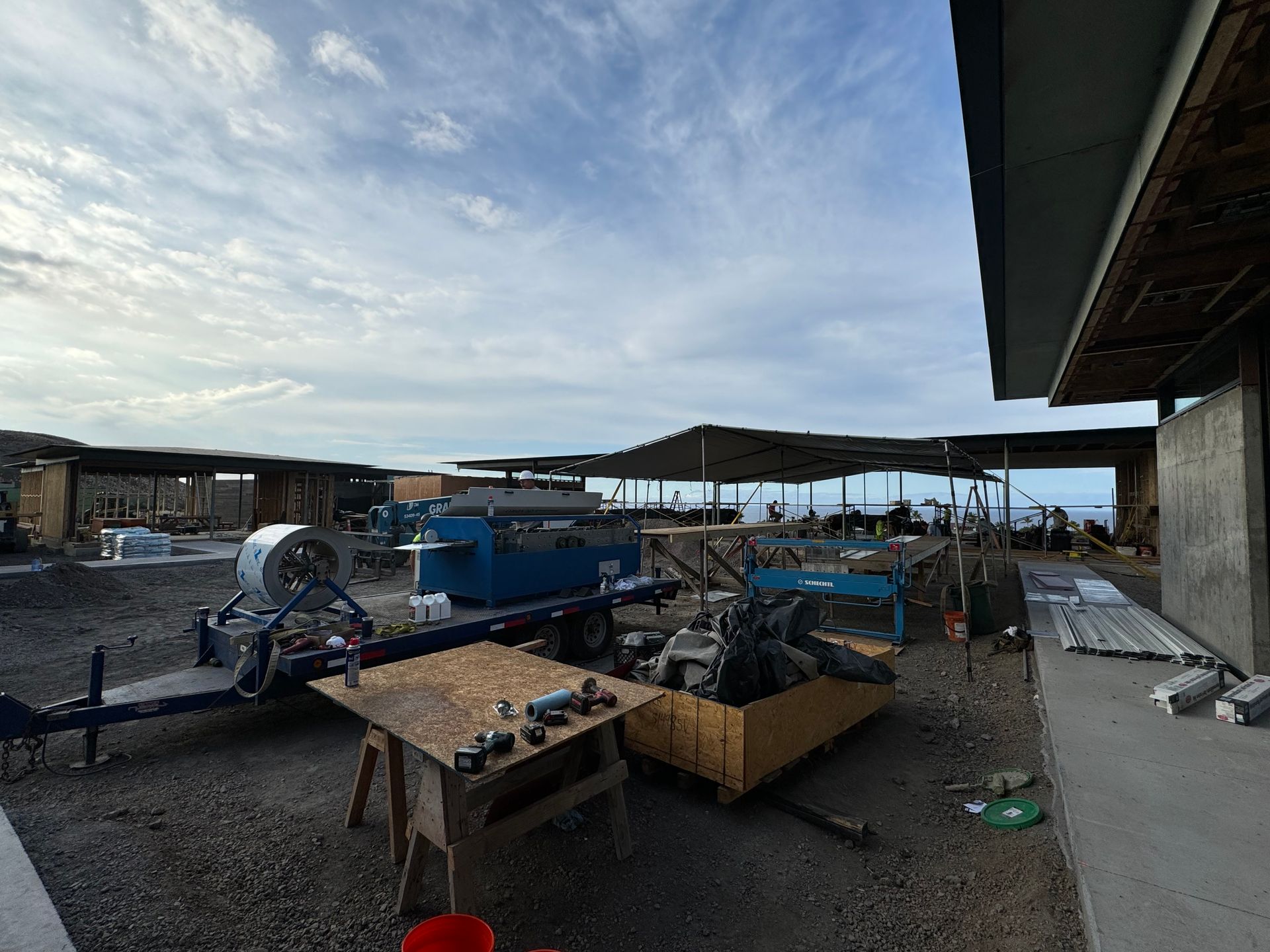 Outdoor worksite with blue machinery and wooden tables under a partly cloudy sky