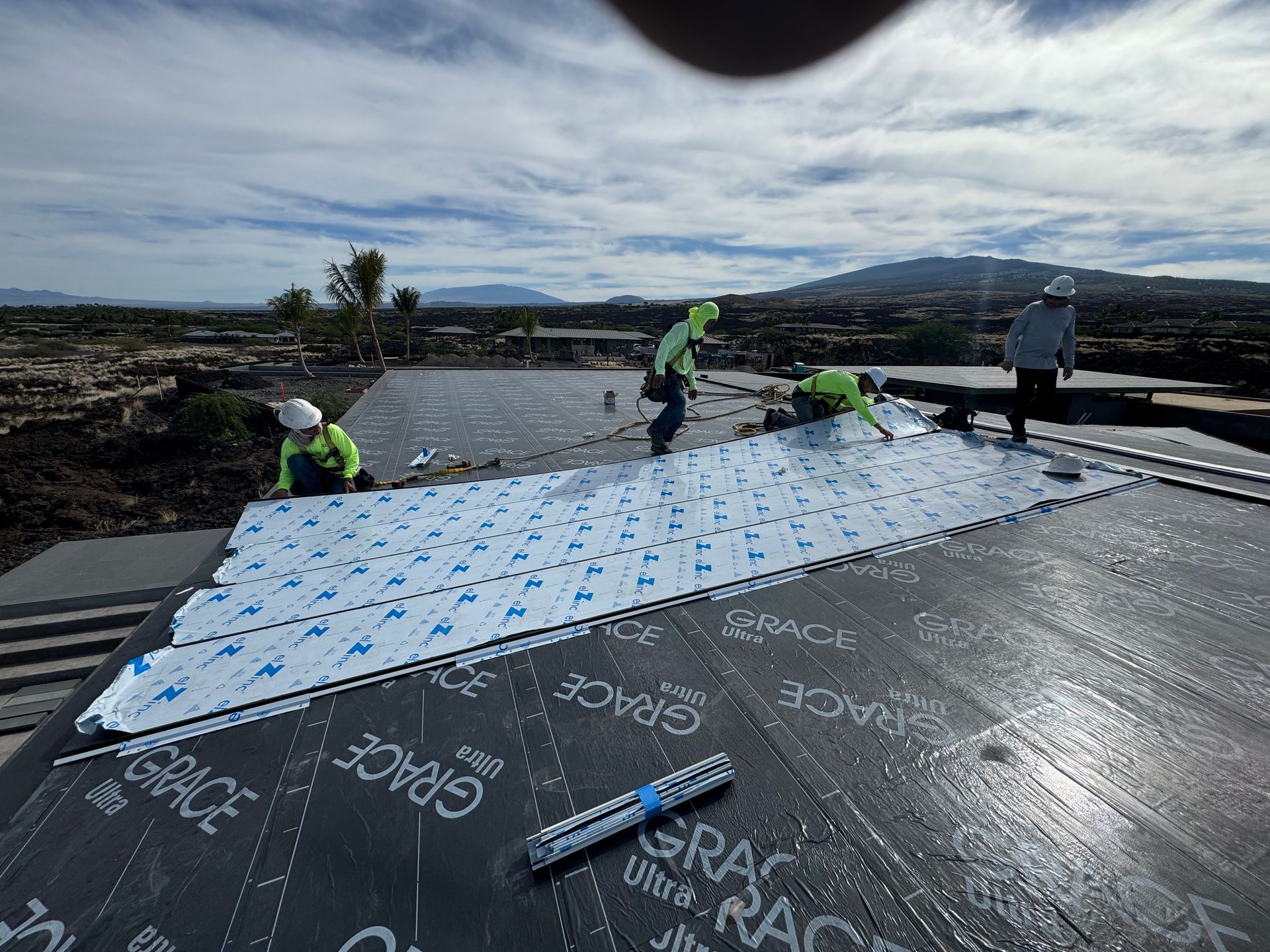 Workers installing a large blue-and-white sheet on a rooftop at a construction site