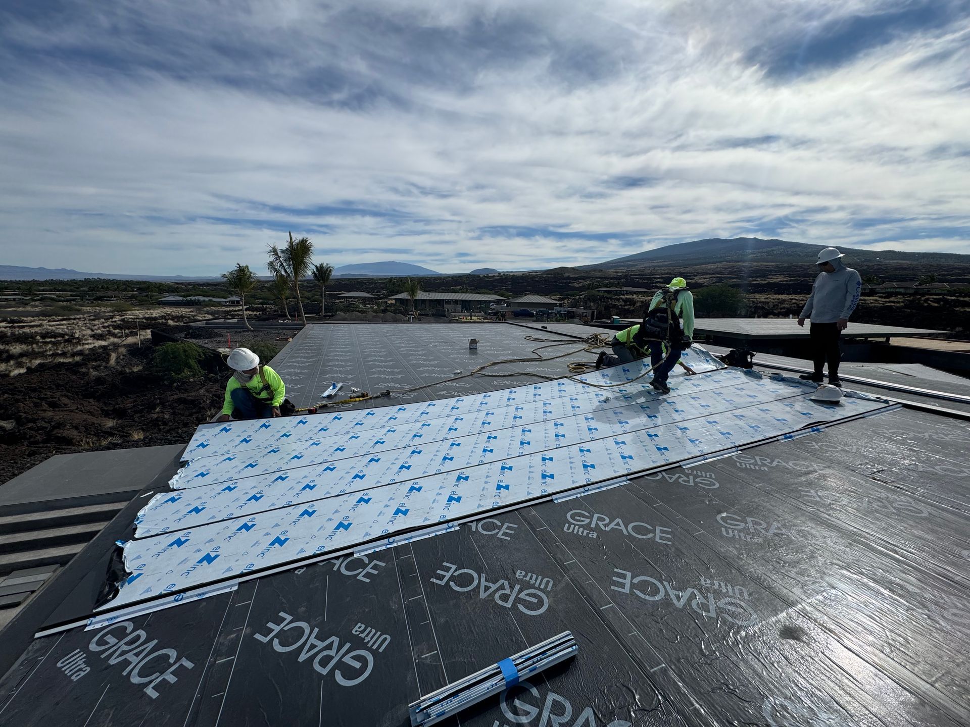 Workers installing roofing underlayment on a sloped roof with cloudy sky overhead