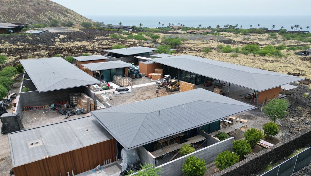 Aerial view of a modern coastal property with gray roofs, courtyard, and ocean in the background