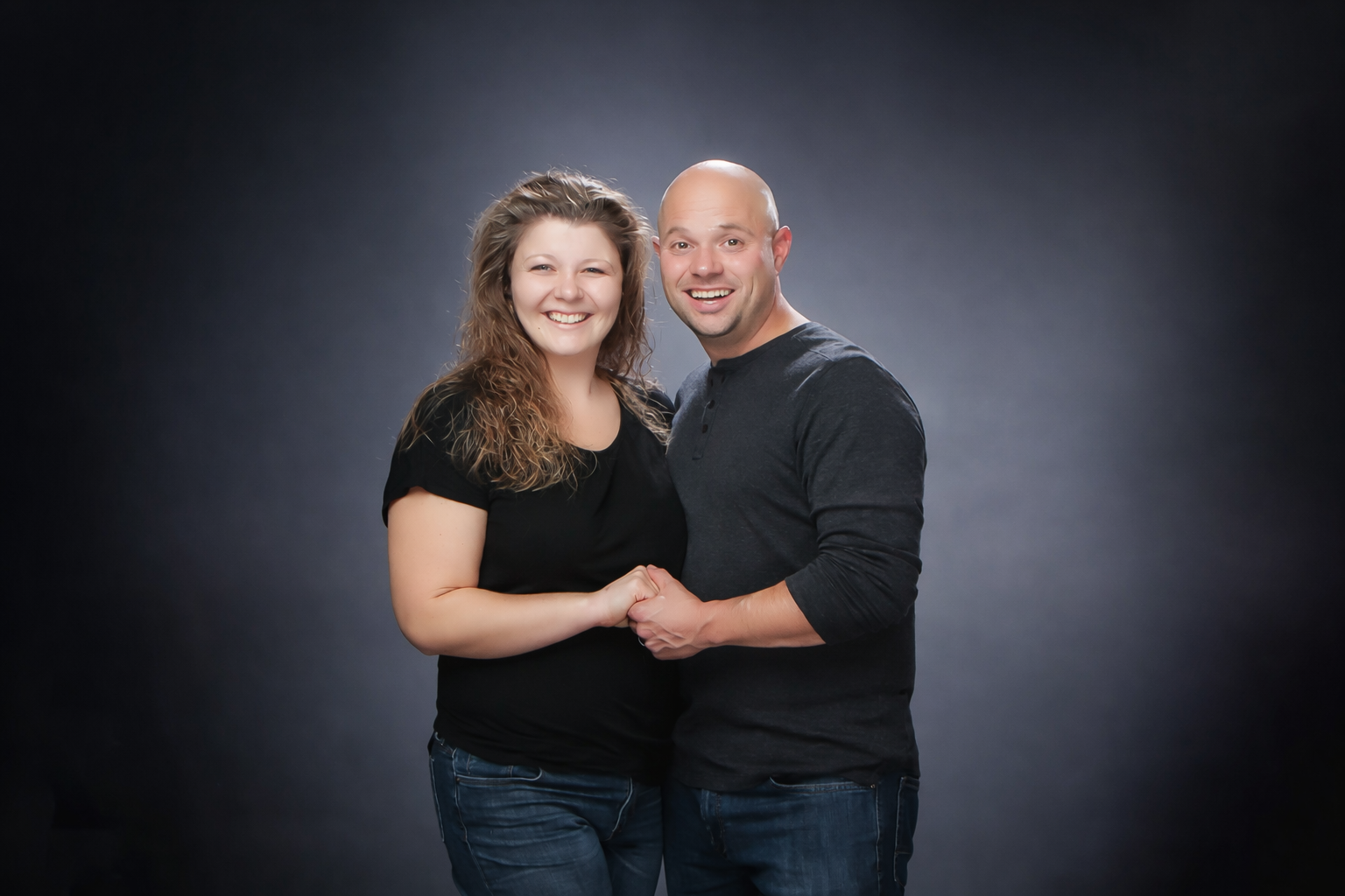 Two people standing close together, smiling against a dark studio backdrop
