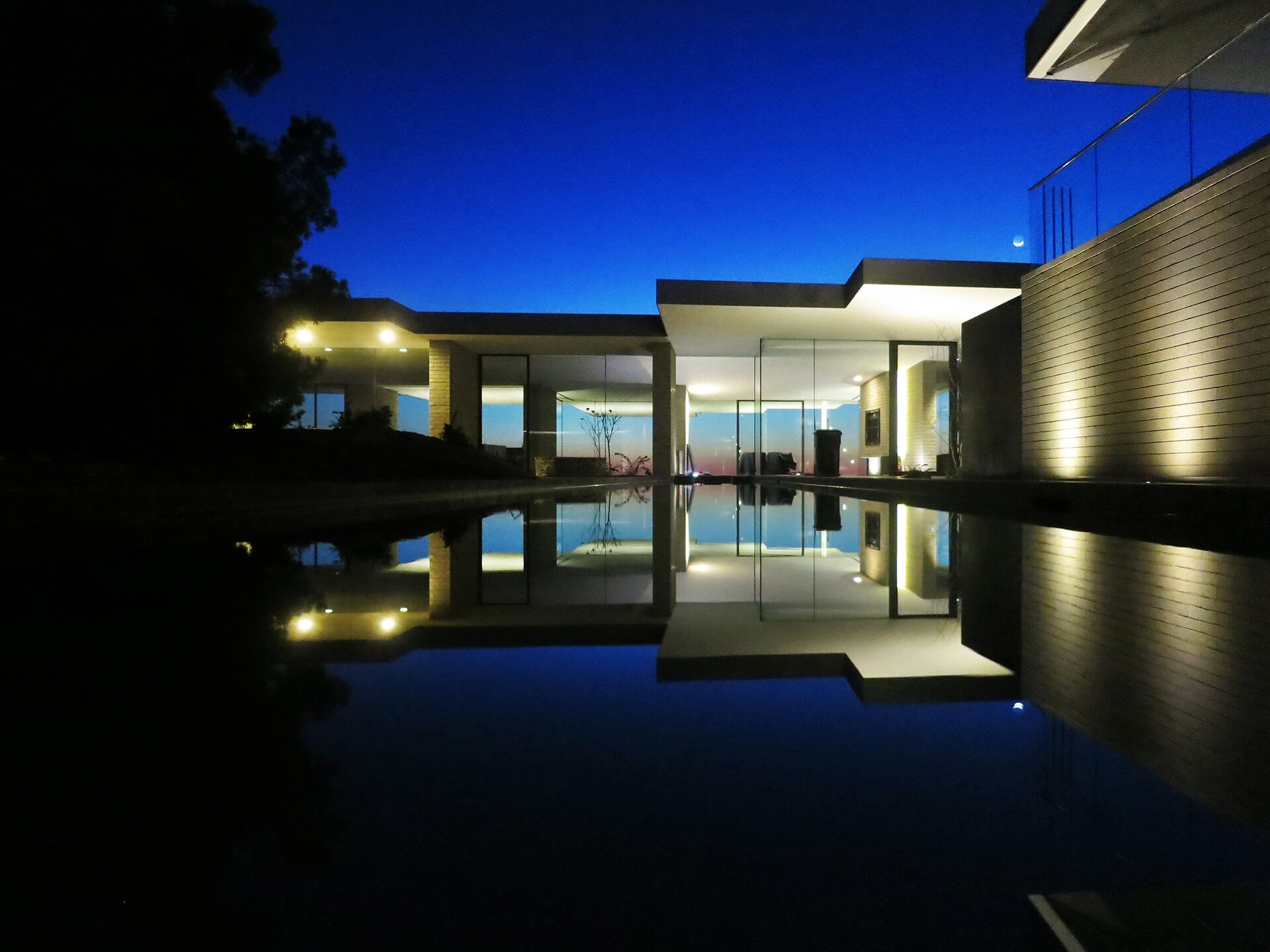 Modern house at night reflected in a still pool, with warm interior lights and deep blue sky