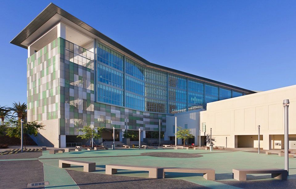 Modern glass-and-concrete office building with a courtyard and benches under a clear blue sky