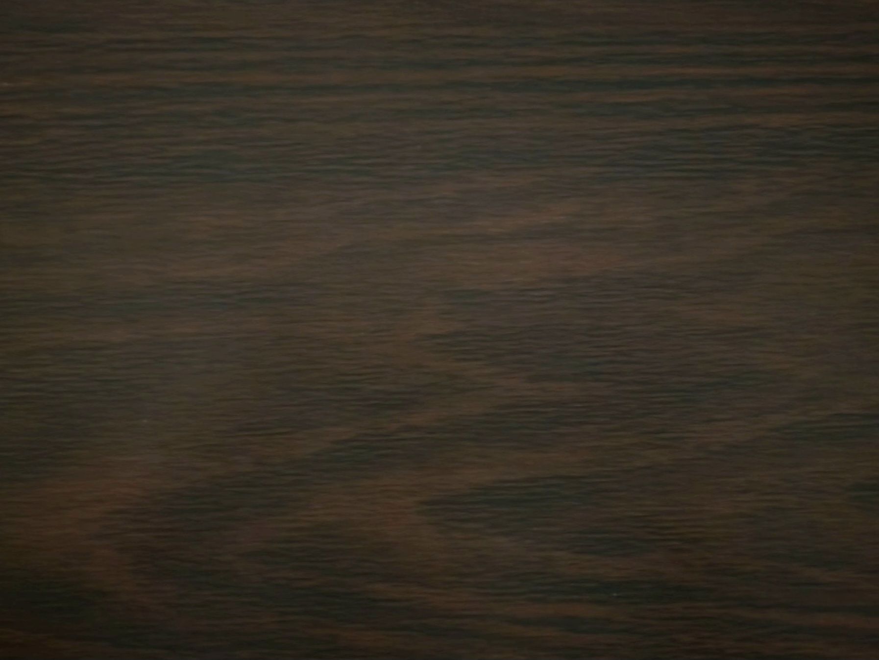 Dark wooden surface with horizontal grain patterns and a blurred greenish reflection in the center