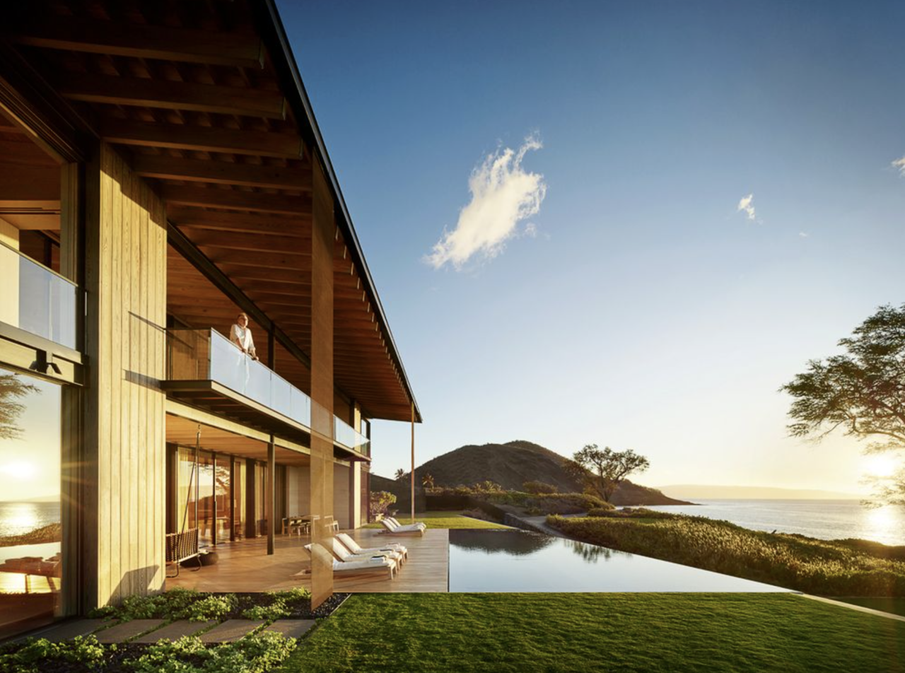 Modern seaside villa with a pool, sunlit deck, and ocean view at sunset