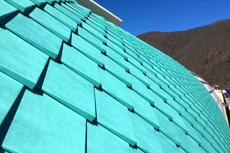 Turquoise shingle roof on a steep slope against a blue sky and distant mountains