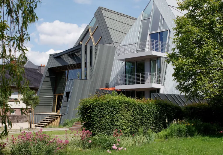 Modern house with angular gray roofs, large windows, and a garden in front