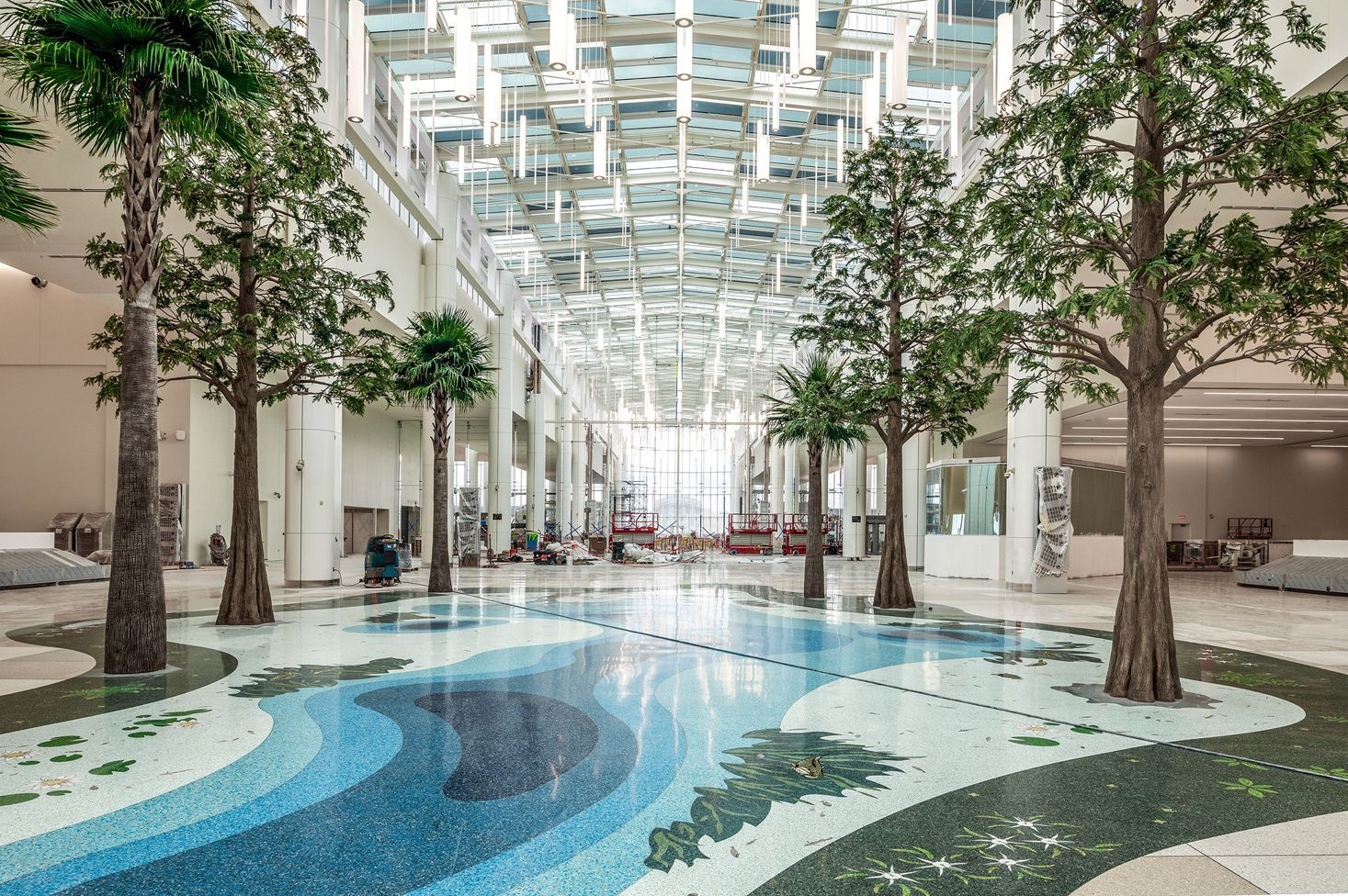 Indoor atrium with a blue patterned floor, tall trees, and a bright skylit ceiling
