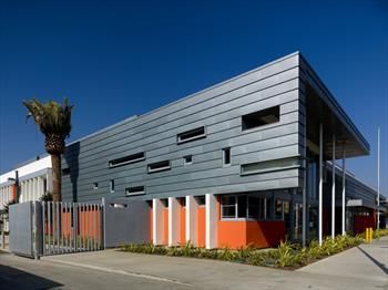 Modern gray commercial building with orange accents and a gated entrance under a blue sky