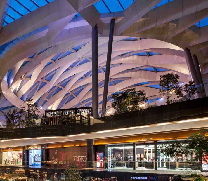 Modern shopping mall with sculptural white canopy and blue-lit roof at dusk, storefronts below