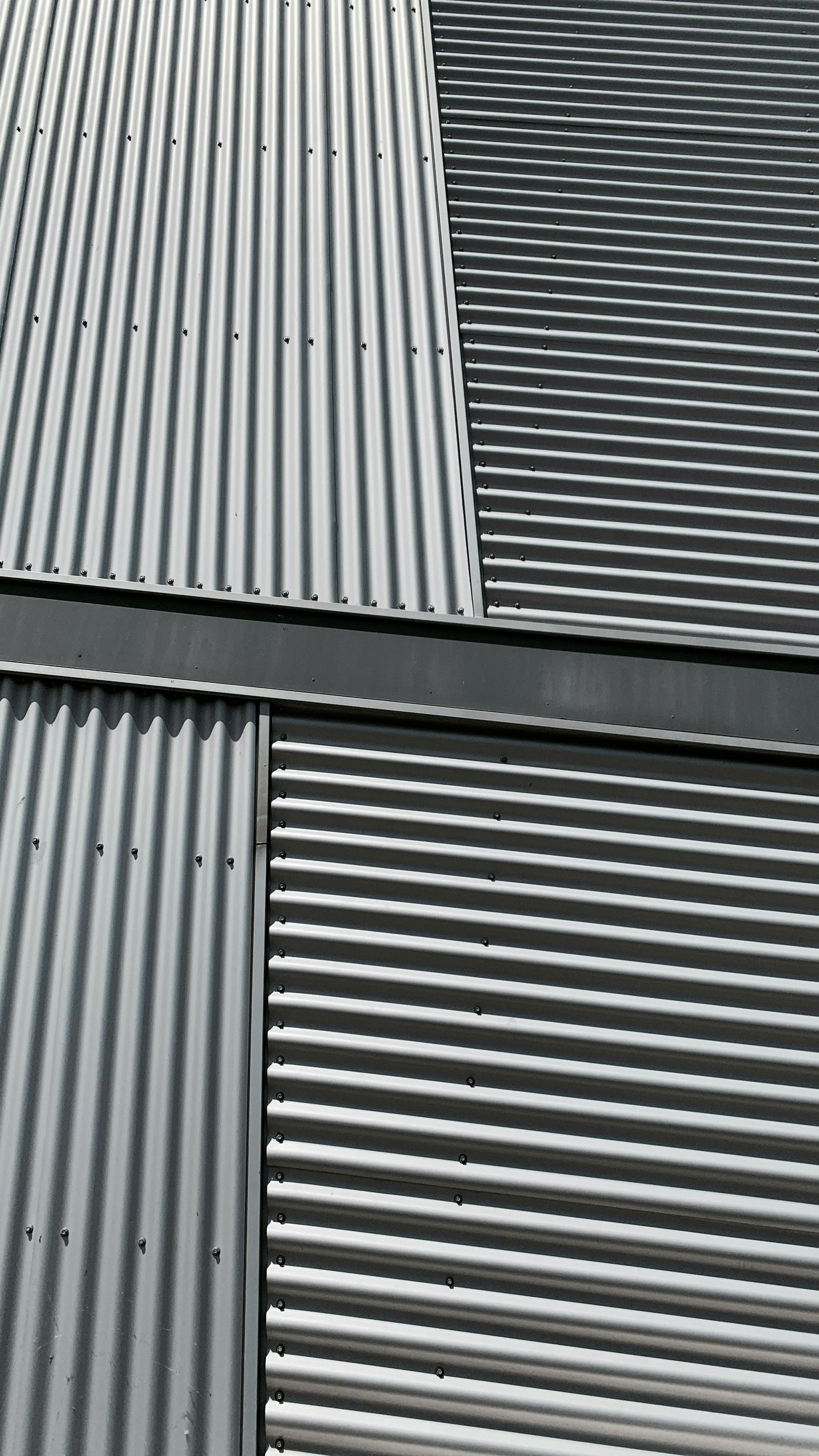 Gray corrugated metal wall panels with diagonal and horizontal ridges, forming a geometric pattern
